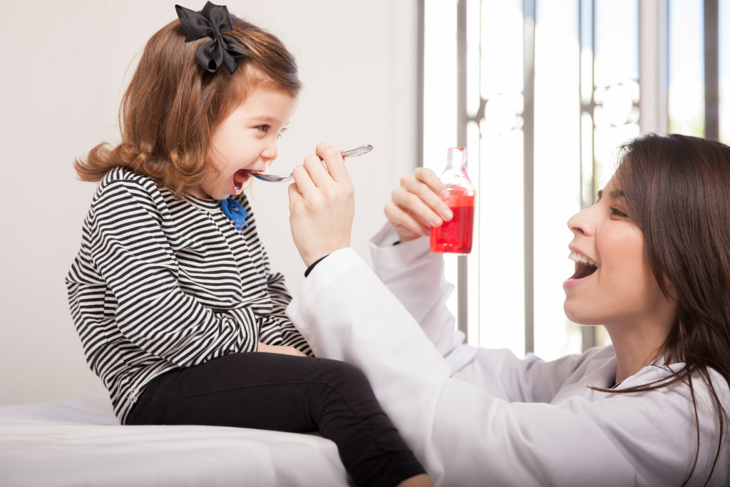 35814424 - pretty pediatrician giving some cough syrup to a little girl in her office